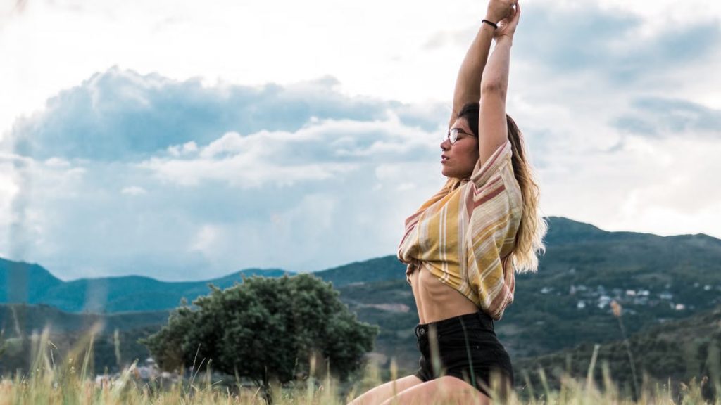 Woman practicing yoga pose in a scenic outdoor field with mountains.